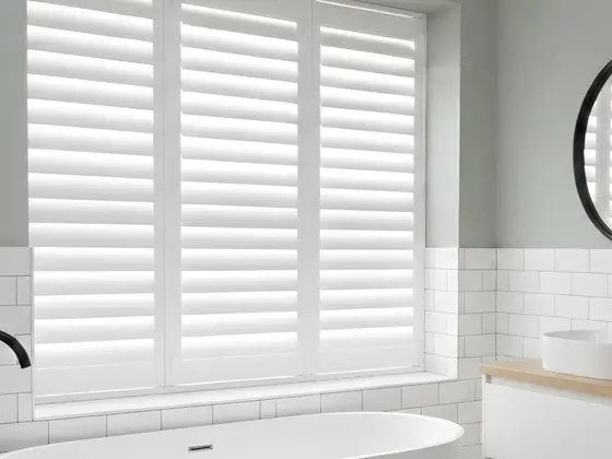 Full-height white Tonga shutters over a freestanding bath in a tiled bathroom.