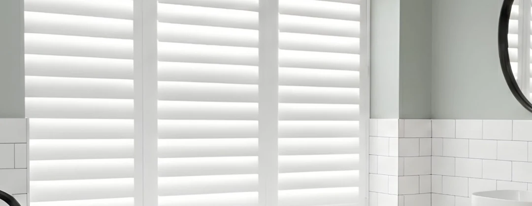 Full-height white Tonga shutters over a freestanding bath in a tiled bathroom alcove.