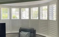 Interior view of white plantation shutters fitted across a three-section bay window.