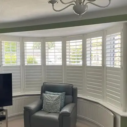 Interior view of white plantation shutters fitted across a three-section bay window.