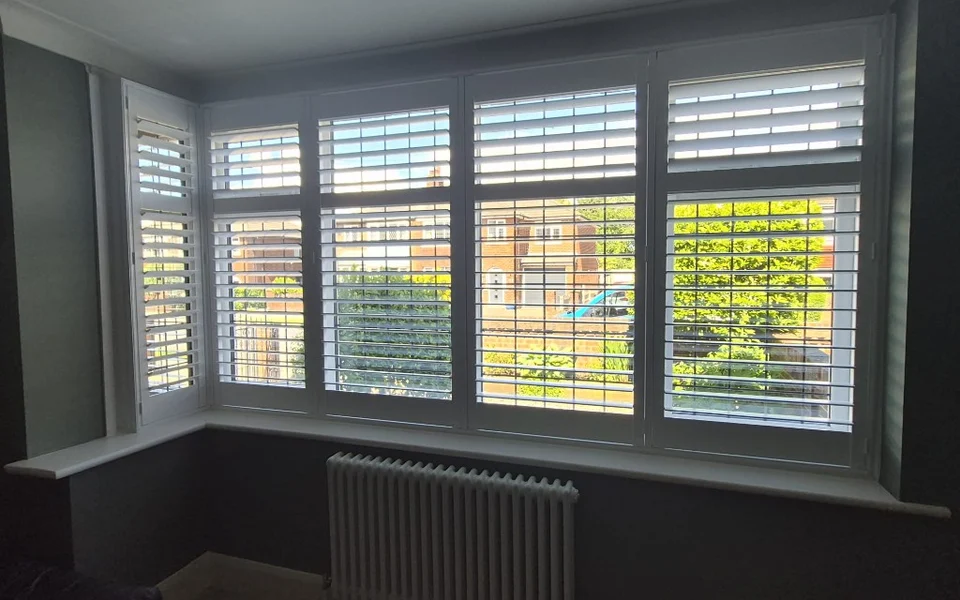 Straight-on view of white plantation shutters on a Bolton lounge bay with charcoal walls and column radiator.