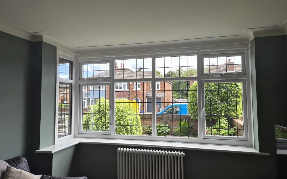 Lounge bay in Bolton before shutters, white framed windows with leaded rectangular glazing and a white column radiator below the sill.