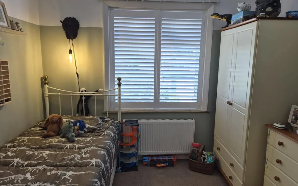 Same Brighouse bedroom after two white full-height plantation shutter panels were fitted in the recess, louvres open for daylight.