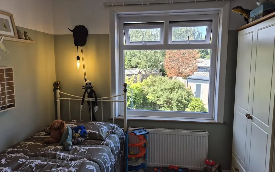 Brighouse bedroom before shutters, white uPVC window above a radiator beside a single bed and wardrobe, with a bare curtain track above the frame.