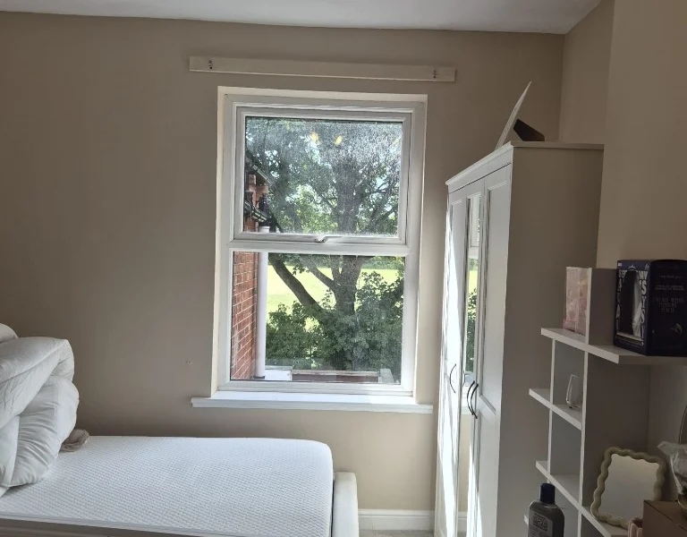 Castleford bedroom before shutters, showing a bare white uPVC window with a wooden batten above and a mirrored wardrobe to the side.