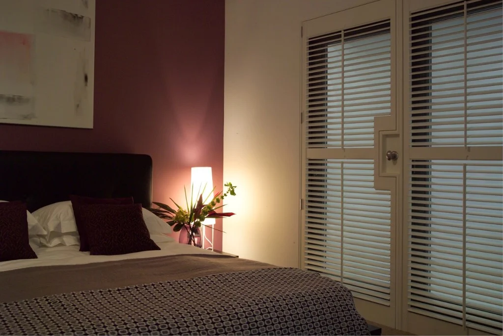 White French door shutters providing privacy in a softly lit bedroom.