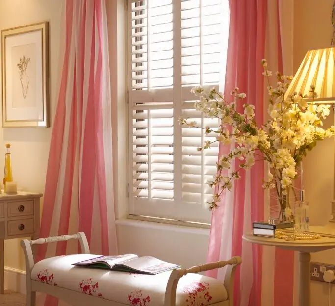 Full-height white plantation shutters in a bright bedroom with independent louvre control.