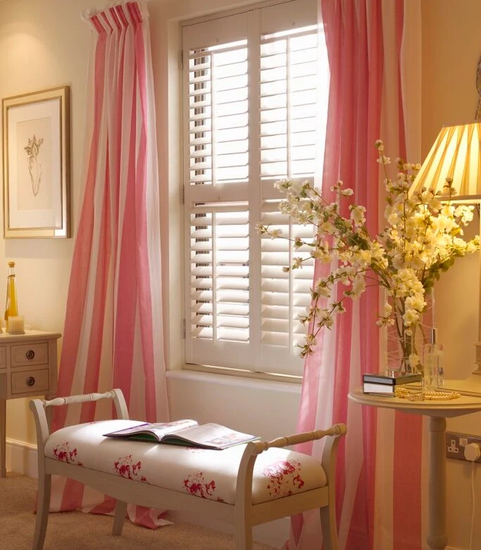Full-height white plantation shutters in a bright bedroom with independent louvre control.