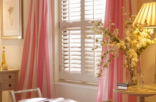 Full-height white plantation shutters in a bright bedroom with independent louvre control.