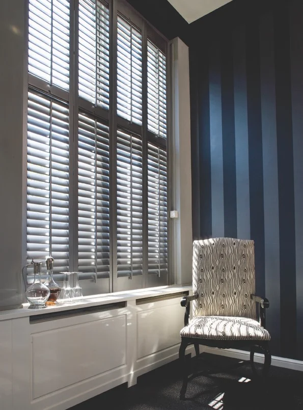 Grey full height shutters in a tall-window lounge.