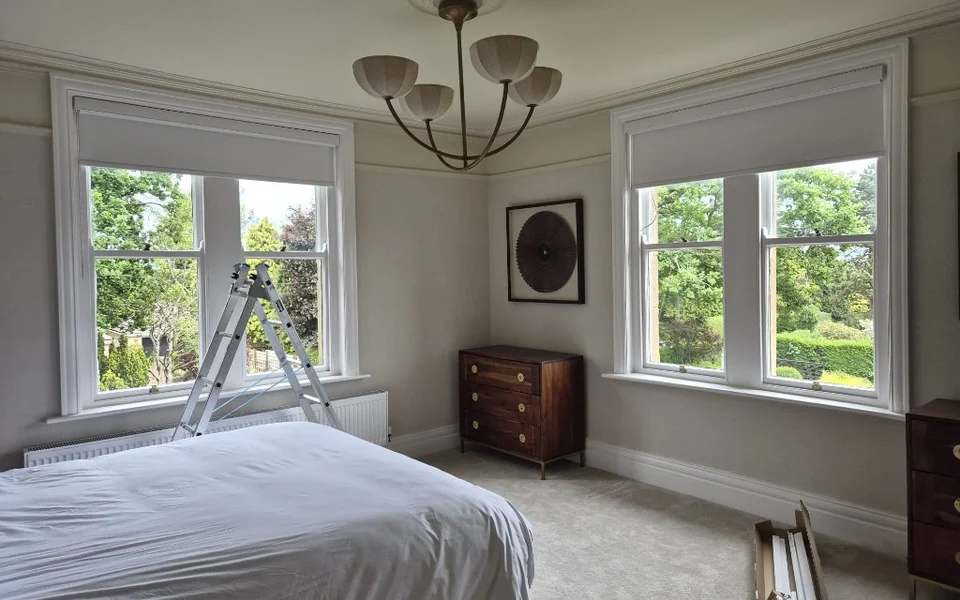 Harrogate bedroom during shutter installation, with ladder, packaging, and roller blinds still on the windows.