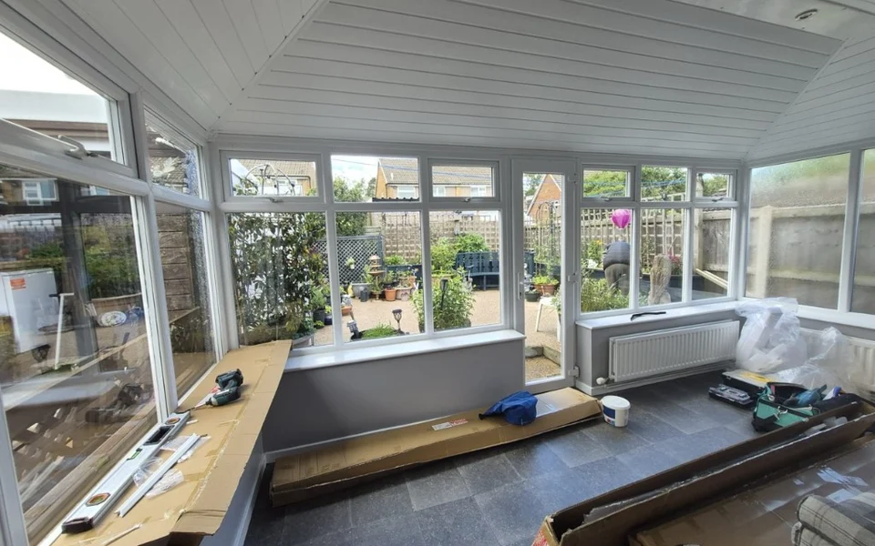 Harrogate conservatory before shutters and blinds, with packaging and tools on the tiled floor.