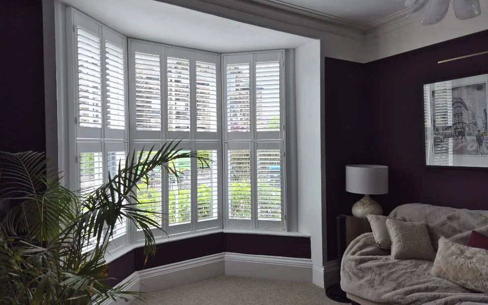 Wide view of Harrogate lounge with tier-on-tier bay shutters, deep purple walls, and neutral sofa.
