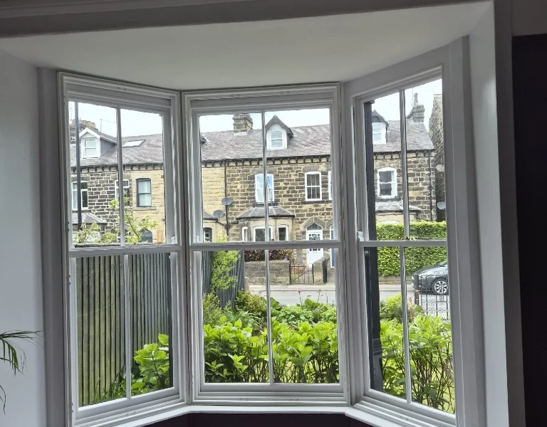 Harrogate lounge bay window before shutters, white sash frames with garden views and protective dust sheet on the carpet.