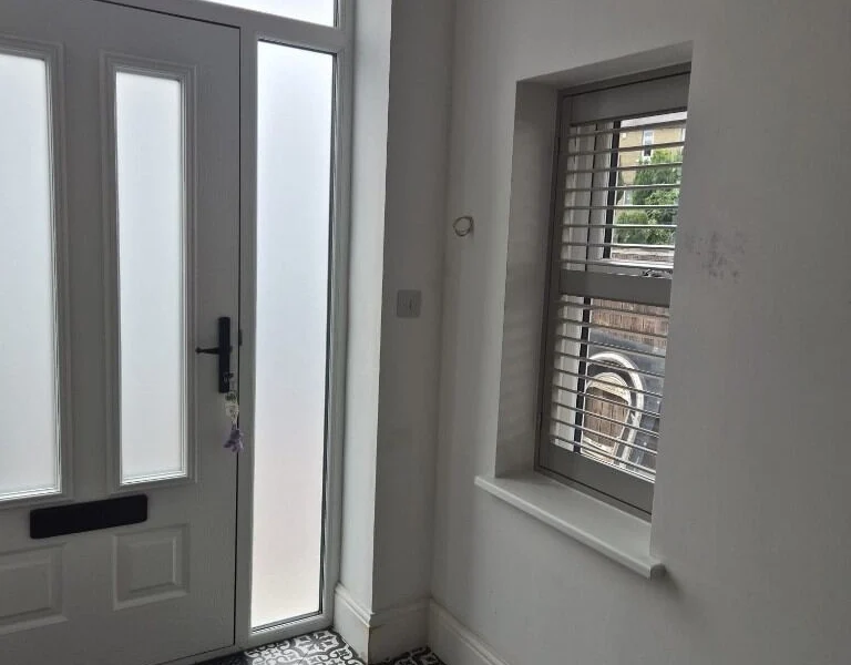 Huddersfield hallway after a light grey plantation shutter was fitted in the recessed window beside the front door, above black and white patterned floor tiles.