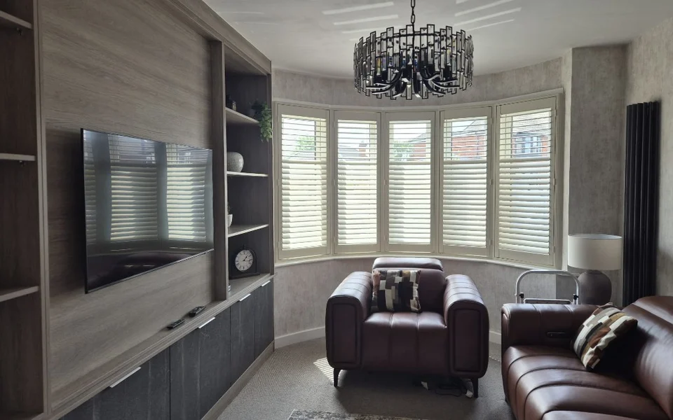 Same Huntington lounge bay after white plantation shutters were fitted across all five panels, louvres closed with a brown leather armchair in front.