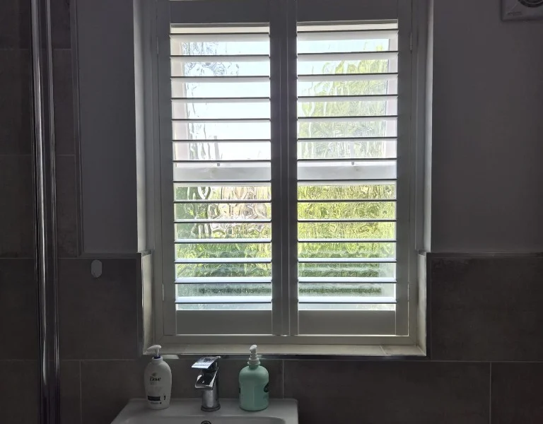 Ilkley bathroom with white plantation shutters fitted above the basin, louvres open over frosted glass.