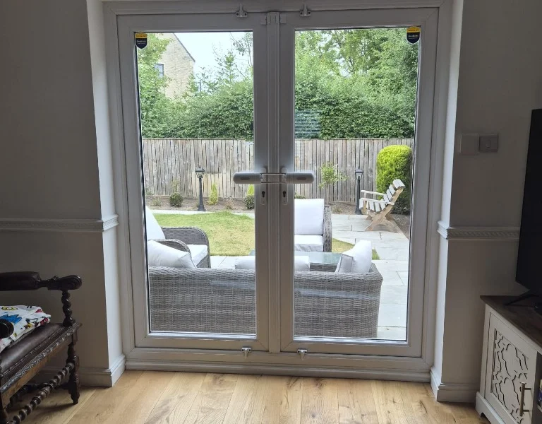 Ilkley lounge patio doors before shutters, white double doors to the garden with a white track component on the wooden floor.