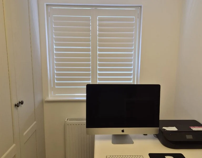 Ilkley home office with white plantation shutters on the window behind a desk and computer.