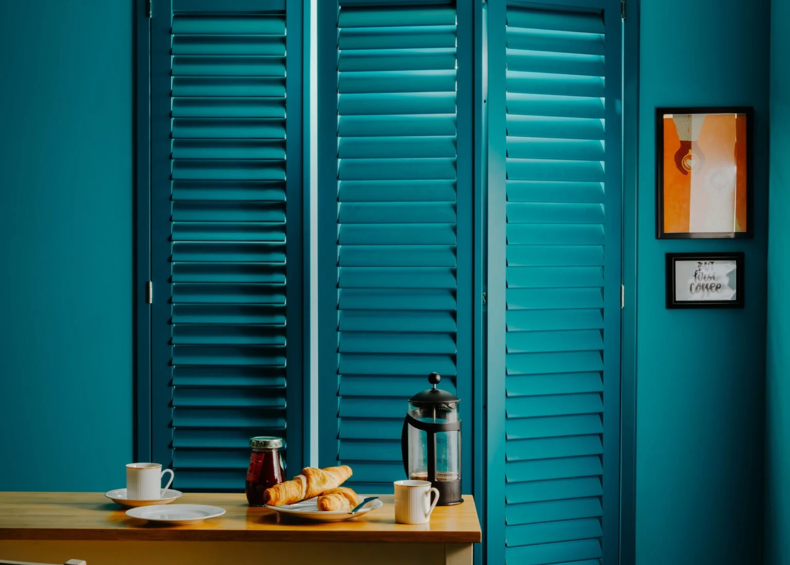 Teal colour-matched Java shutters on a dining-room window with breakfast table in the foreground.