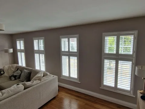 Four white full-height plantation shutters with mid-rails in a modern living room