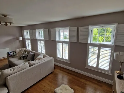 White tier-on-tier plantation shutters across four living room windows, top panels folded open