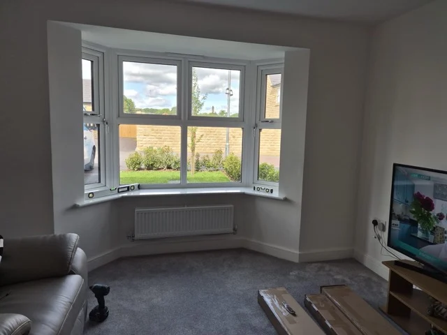 Otley lounge bay during shutter installation, with spirit levels on the sill and shutter packaging on the carpet.