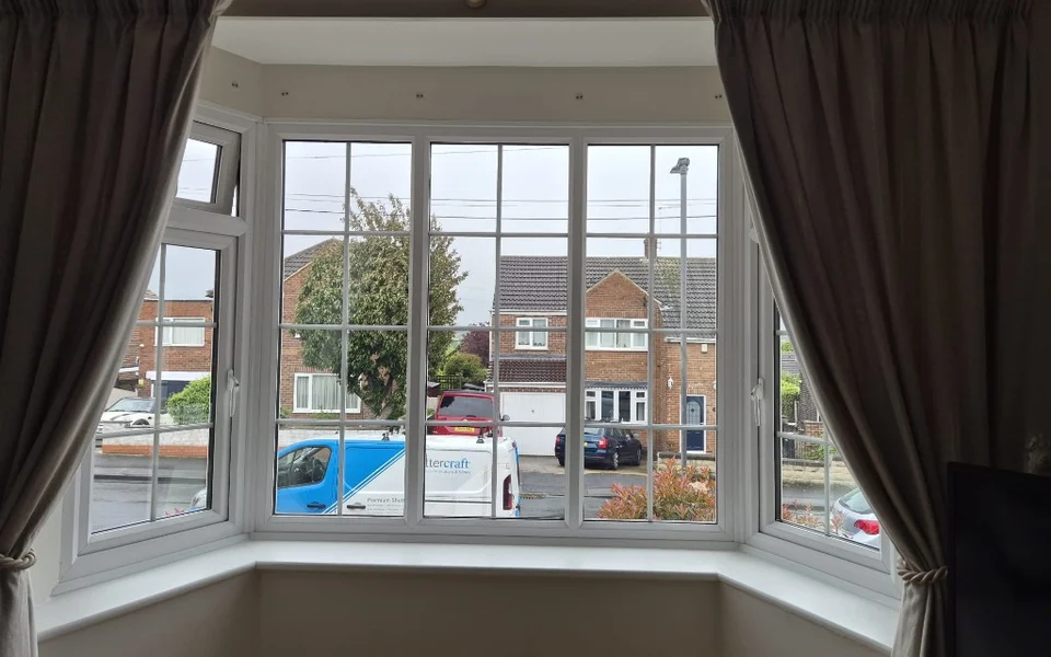 Interior view through the same Pontefract lounge bay toward brick houses, parked cars, and an overcast sky.