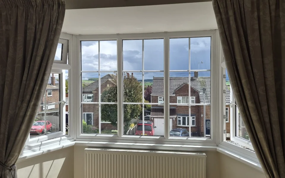 Lounge bay window in Pontefract before shutters, showing white uPVC frames with Georgian bars and neutral curtains drawn to the sides.