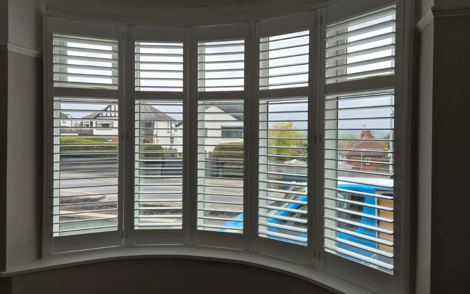 Curved five-panel bay window in Rawdon fitted with white full-height plantation shutters with mid-rails.