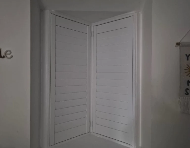 Same V-shaped window in Rawdon with white plantation shutters closed for near-blackout light control.
