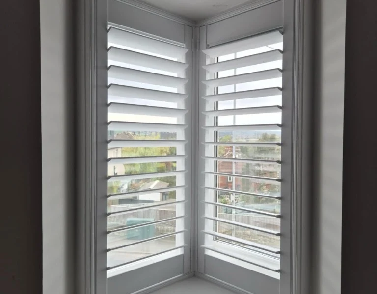White plantation shutters on a V-shaped corner window in Rawdon with louvres tilted open for daylight.