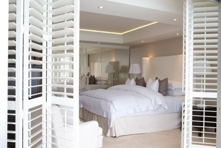 White room divider shutters between a bedroom and adjoining dressing area.