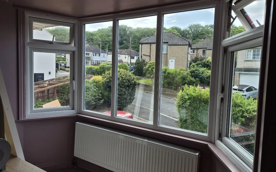 Shipley bedroom bay window before shutters, five-panel white uPVC bay with mauve walls.