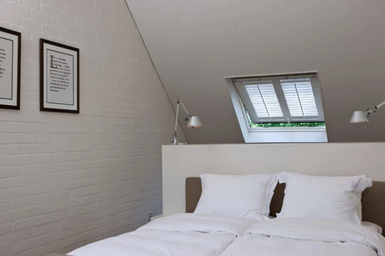 Loft bedroom with skylight shutters fitted above the bed.