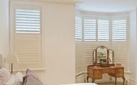 White plantation shutters fitted to a curved bay window, showing clean lines and even louvres.