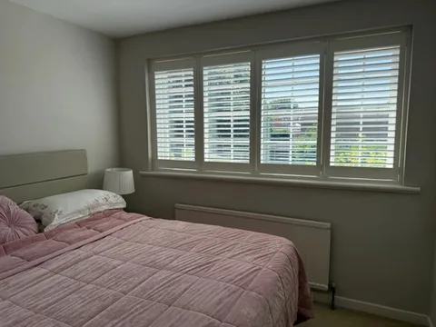 White full-height plantation shutters across a bedroom window with louvres tilted open