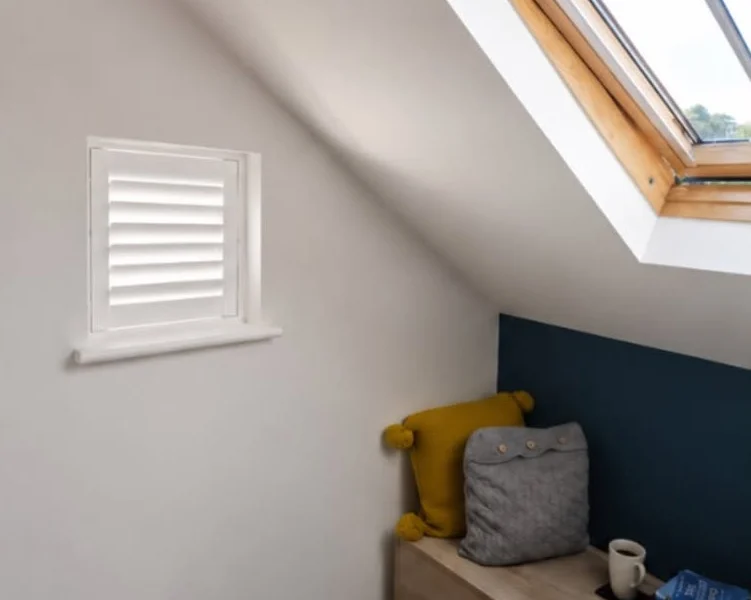 Same Wakefield attic recess after a single white plantation shutter was fitted, louvres tilted for filtered light beside the timber skylight.