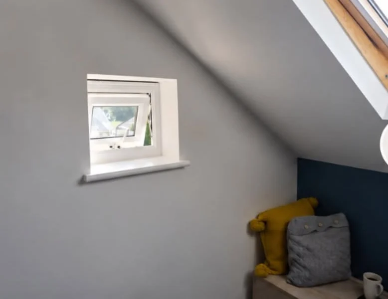 Wakefield attic room before shutters, small square recessed window open beside a timber skylight, with a navy feature wall and cushions below.