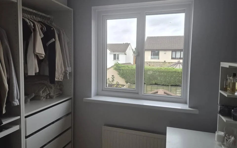 Wakefield bedroom dressing area before shutters, showing a white uPVC window above a radiator beside an open wardrobe and vanity desk.
