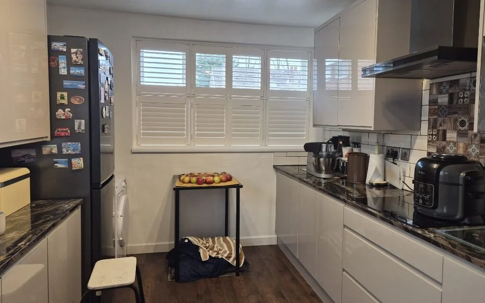 Closer view of the white tier-on-tier shutters in the Wakefield kitchen, top tier louvres open and bottom tier closed, beside the hob and patterned splashback.