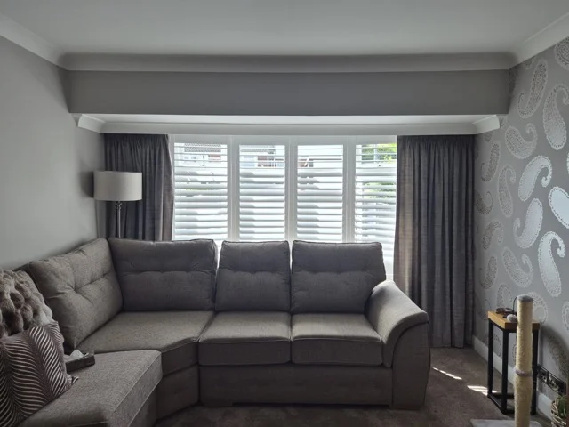 Same Wakefield lounge bay after white plantation shutters were fitted, louvres open with grey curtains.