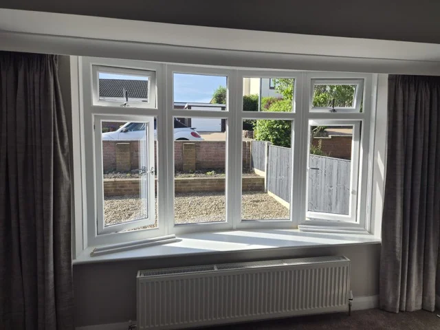 Wakefield lounge bay window before shutters, white uPVC frames with grey curtains.