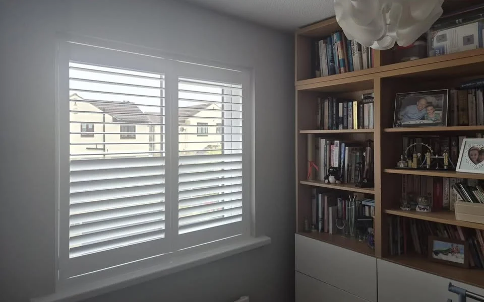 Same Wakefield home office after white full-height plantation shutters were fitted, lower louvres closed and upper louvres open beside a bookcase.