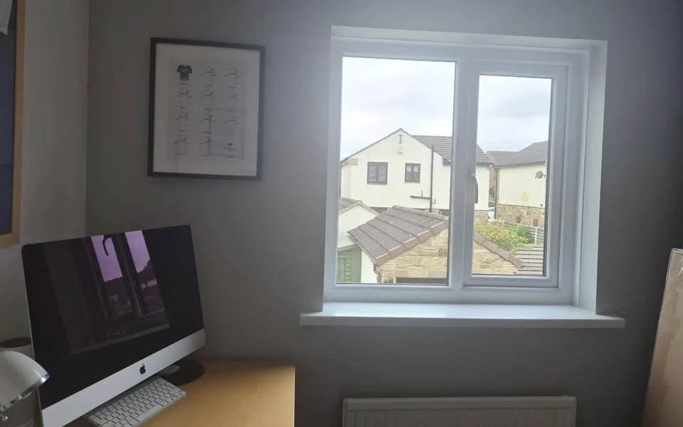Wakefield home office before shutters, white uPVC window above a radiator beside a wooden desk with an iMac.