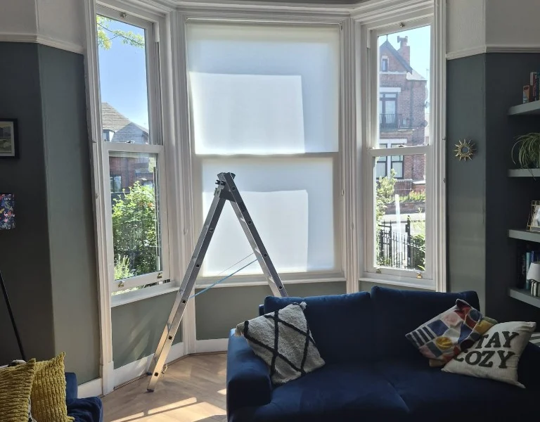 Wakefield lounge bay window before shutters, three-part white uPVC bay with a stepladder during installation and navy sofas.