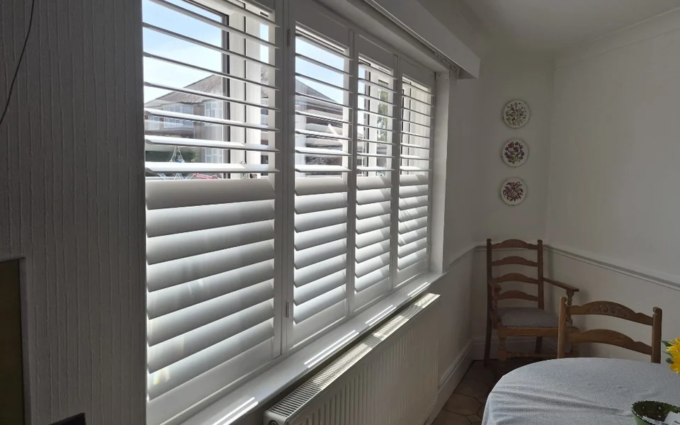 Close view of the York kitchen window with white tier-on-tier shutters, lower louvres closed and upper louvres open for daylight.