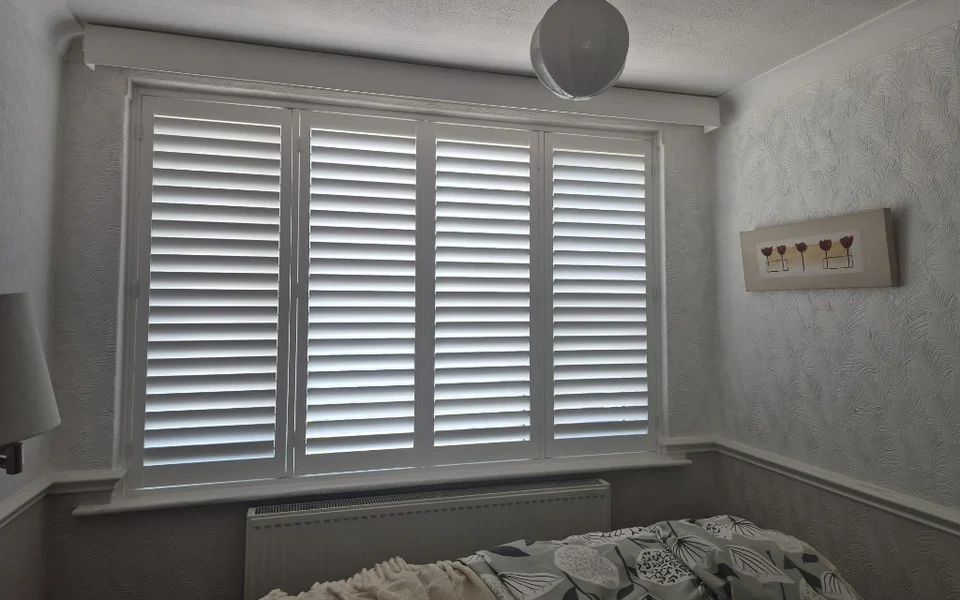 Same York lounge after white full-height plantation shutters were fitted across four panels, louvres open.