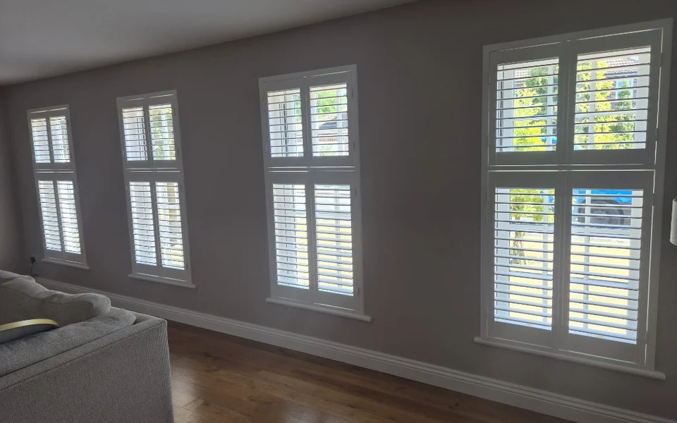 Same York lounge after white tier-on-tier plantation shutters were fitted on all four windows, louvres tilted open.